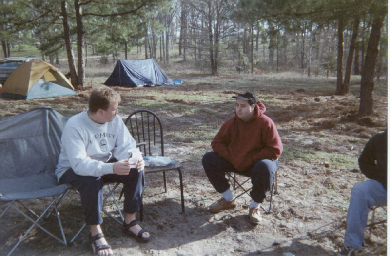 Two campers seated in folding chairs near tents