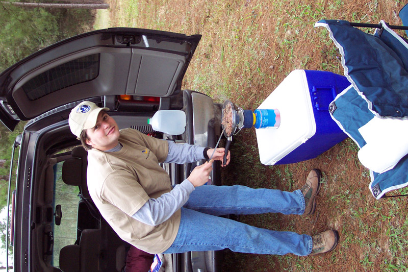 Person seated by an open vehicle and a blue cooler