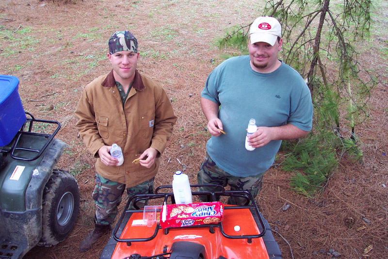 Two people standing beside all-terrain vehicles at camp