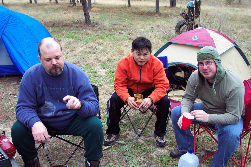 Three people seated in front of tents