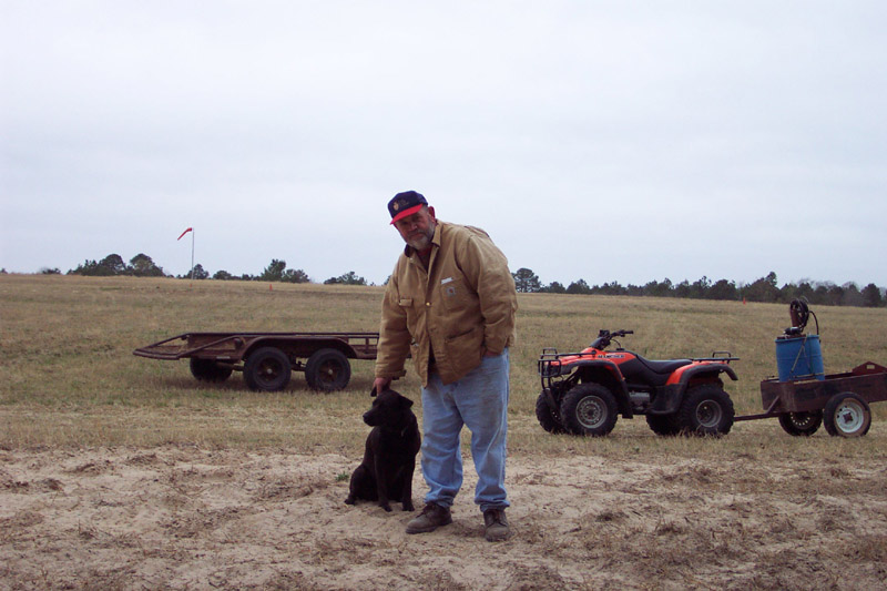 Person and a dog beside vehicles in an open field