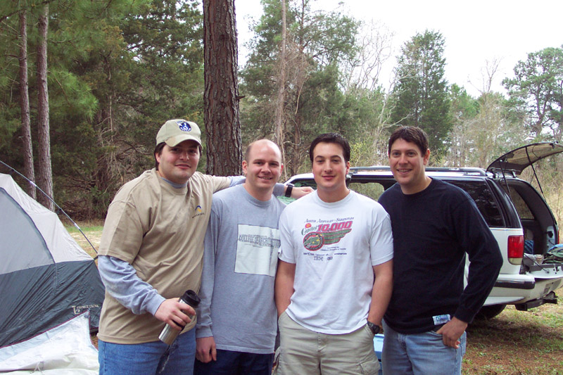 Four people posing together beside a tent and vehicle